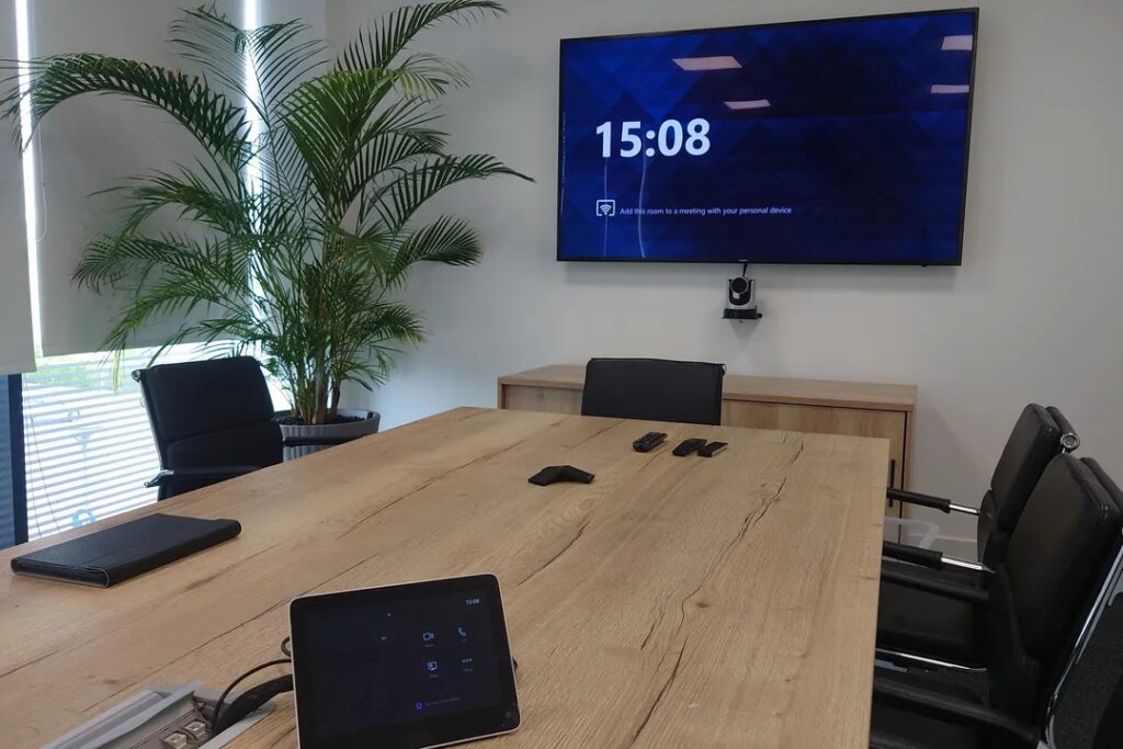 Boardroom with a camera beneath a large format display and a touchpanel on the table.