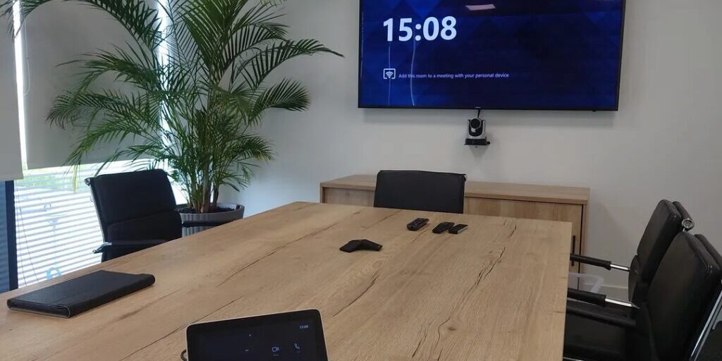 Boardroom with a camera beneath a large format display and a touchpanel on the table.